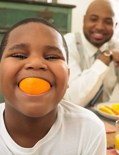 A boy with an orange in his mouth.